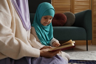 Photo of Muslim woman and her daughter with Quran praying on mat at home