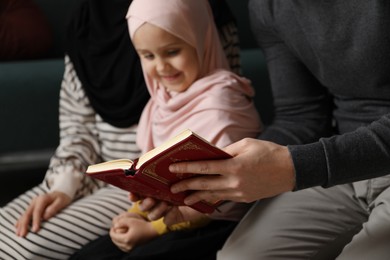 Photo of Muslim family with Quran praying on mat at home, selective focus