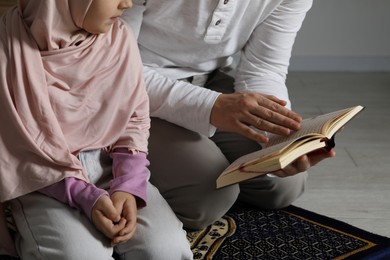 Photo of Muslim man and his daughter with Quran praying on mat at home