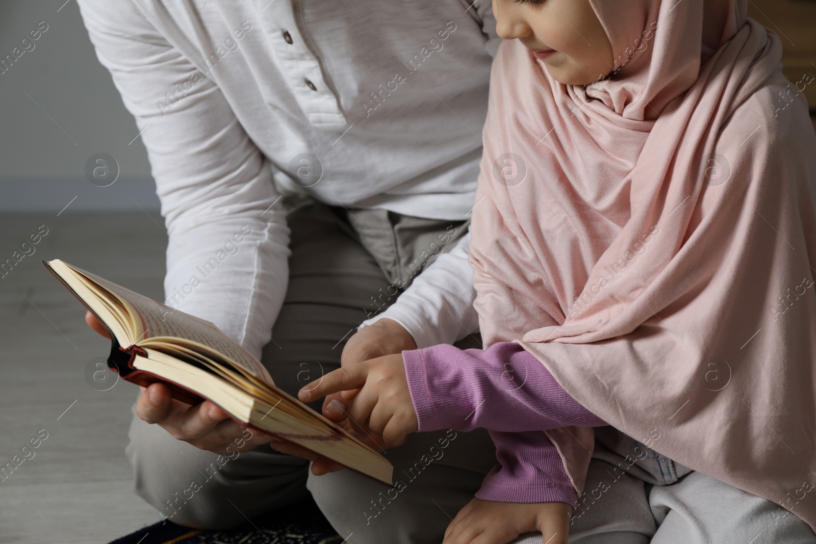 Photo of Muslim man and his daughter with Quran praying on mat at home