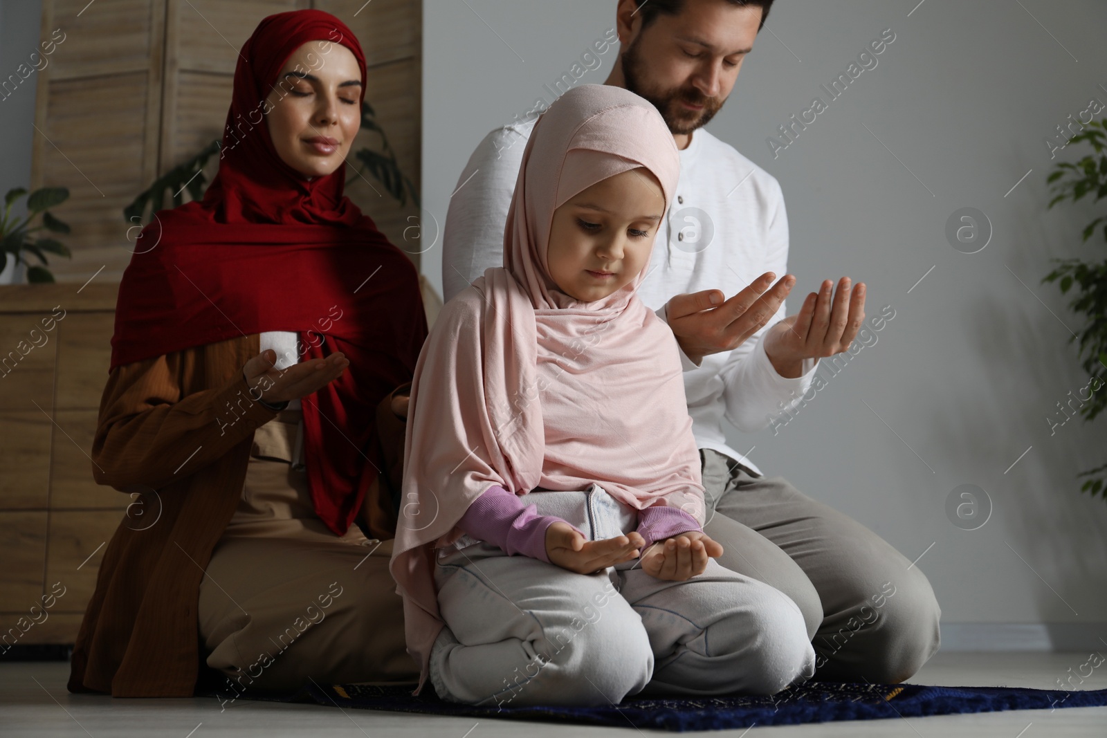 Photo of Muslim family praying on mat at home