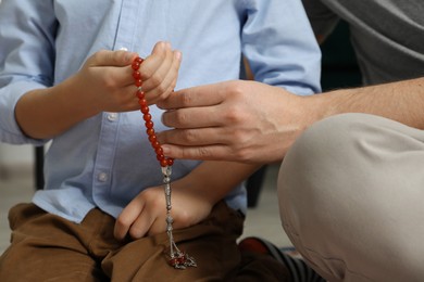 Photo of Muslim man and his son with prayer beads at home, closeup