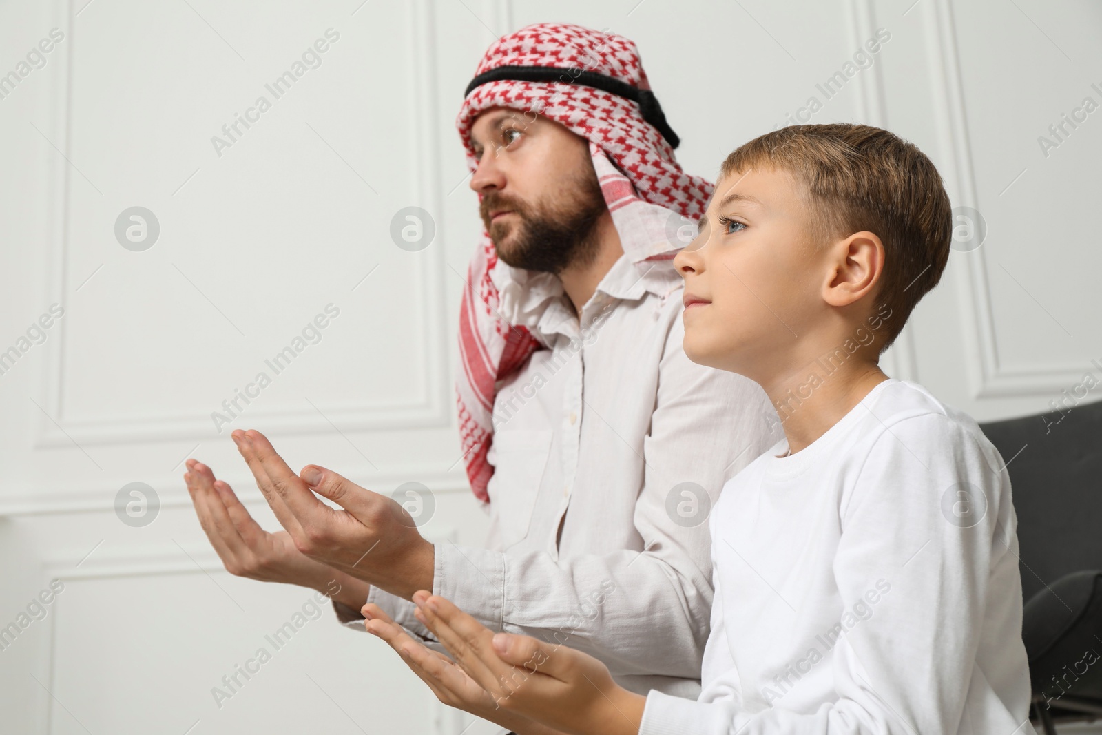 Photo of Muslim man and his son with beads praying indoors, low angle view