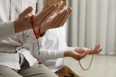 Photo of Muslim man and his son with beads praying indoors, closeup