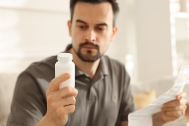 Man with pills and medical instruction at home, selective focus