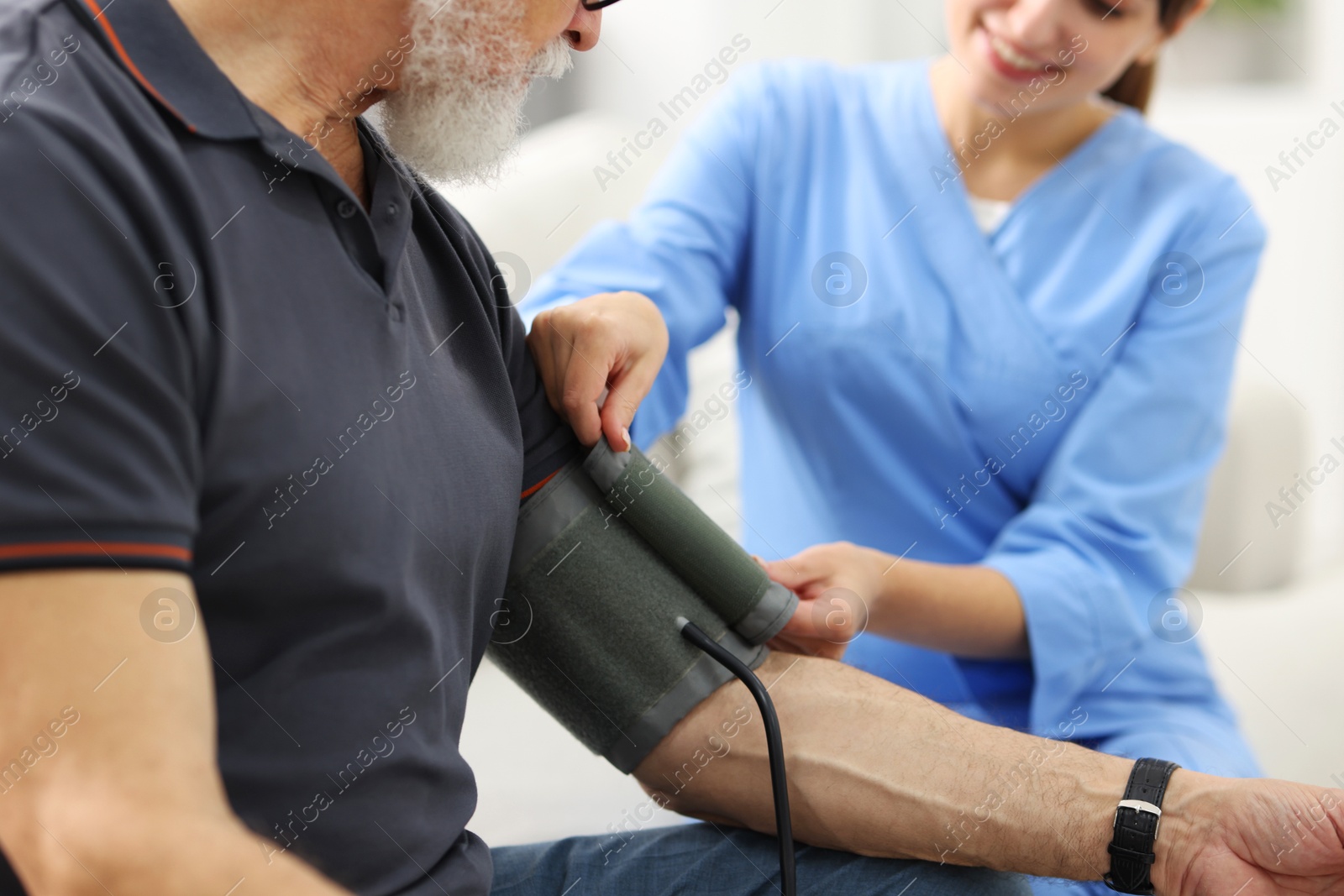 Photo of Nurse measuring senior man's blood pressure at home, closeup