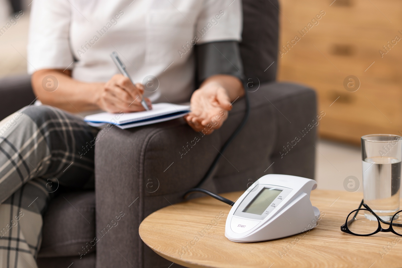 Photo of Senior woman writing results of blood pressure measurement at home, closeup