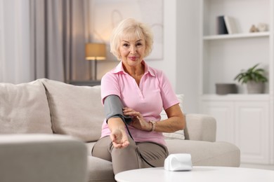 Senior woman measuring blood pressure on sofa at home