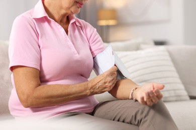 Photo of Senior woman measuring blood pressure on sofa at home, closeup