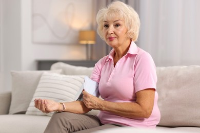 Photo of Senior woman measuring blood pressure on sofa at home. Space for text