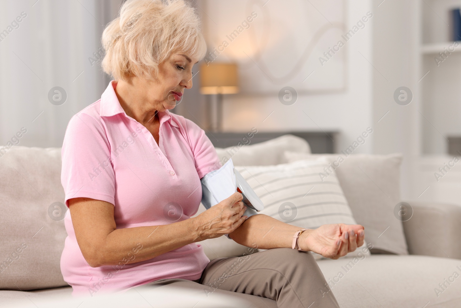 Photo of Senior woman measuring blood pressure on sofa at home. Space for text