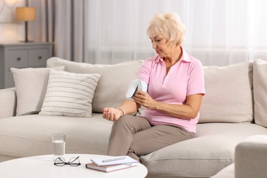 Photo of Senior woman measuring blood pressure on sofa at home