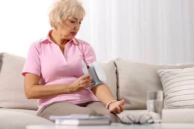 Photo of Senior woman measuring blood pressure on sofa at home. Space for text