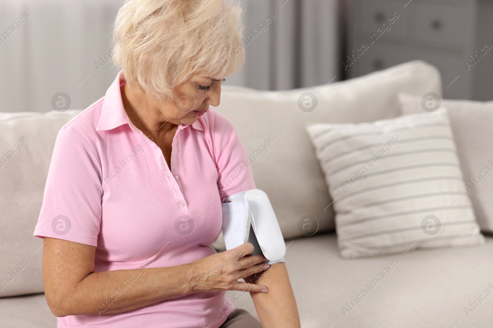 Photo of Senior woman measuring blood pressure on sofa at home. Space for text