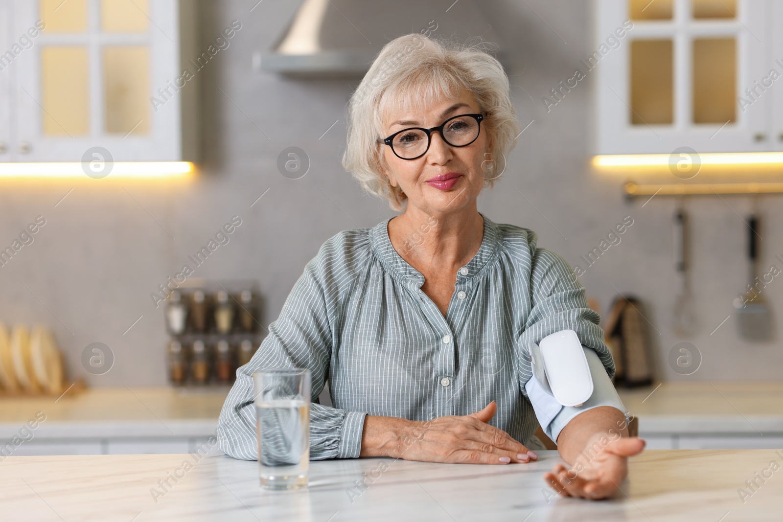 Photo of Senior woman measuring blood pressure at table in kitchen