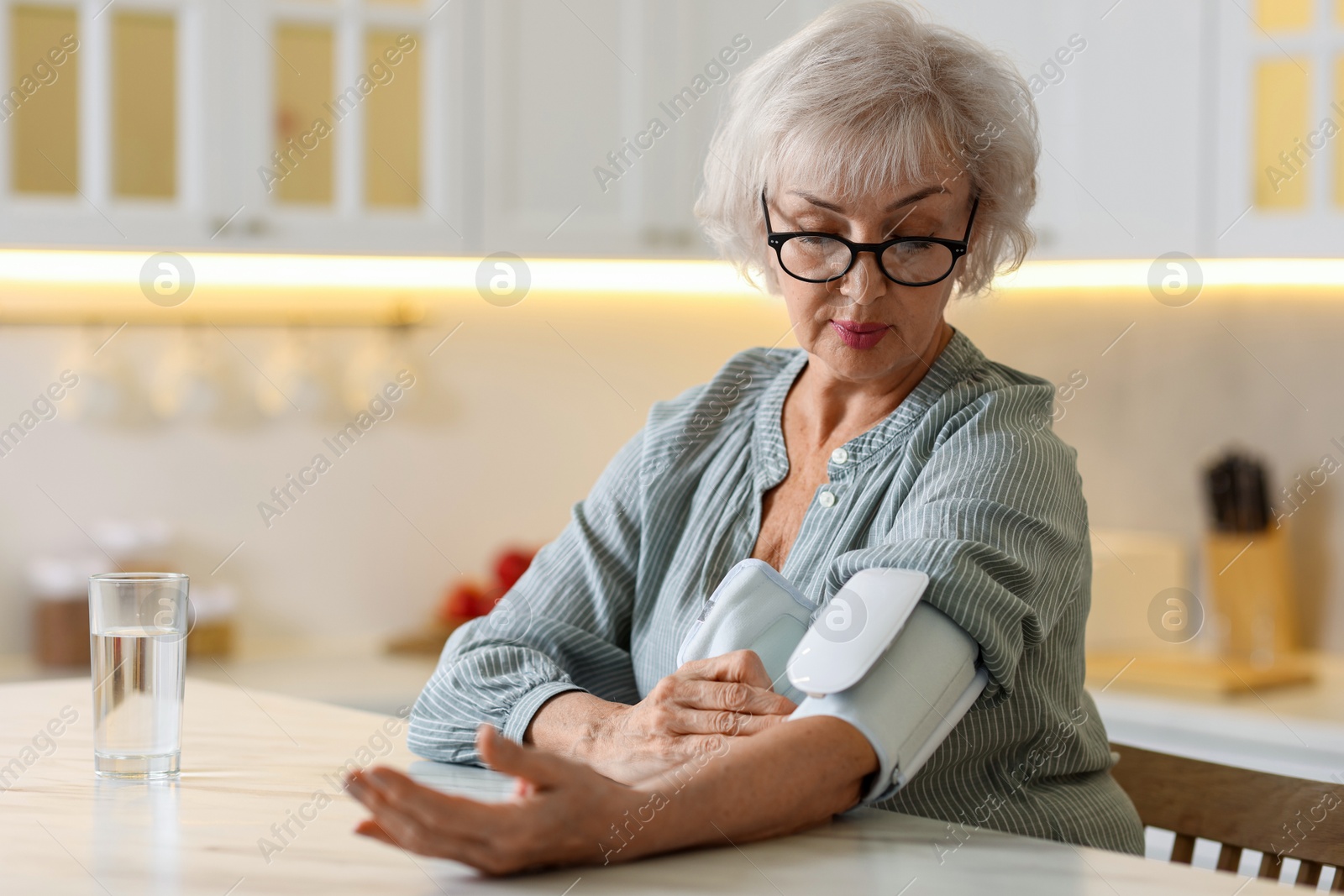 Photo of Senior woman measuring blood pressure at table in kitchen. Space for text