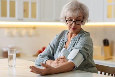 Photo of Senior woman measuring blood pressure at table in kitchen. Space for text