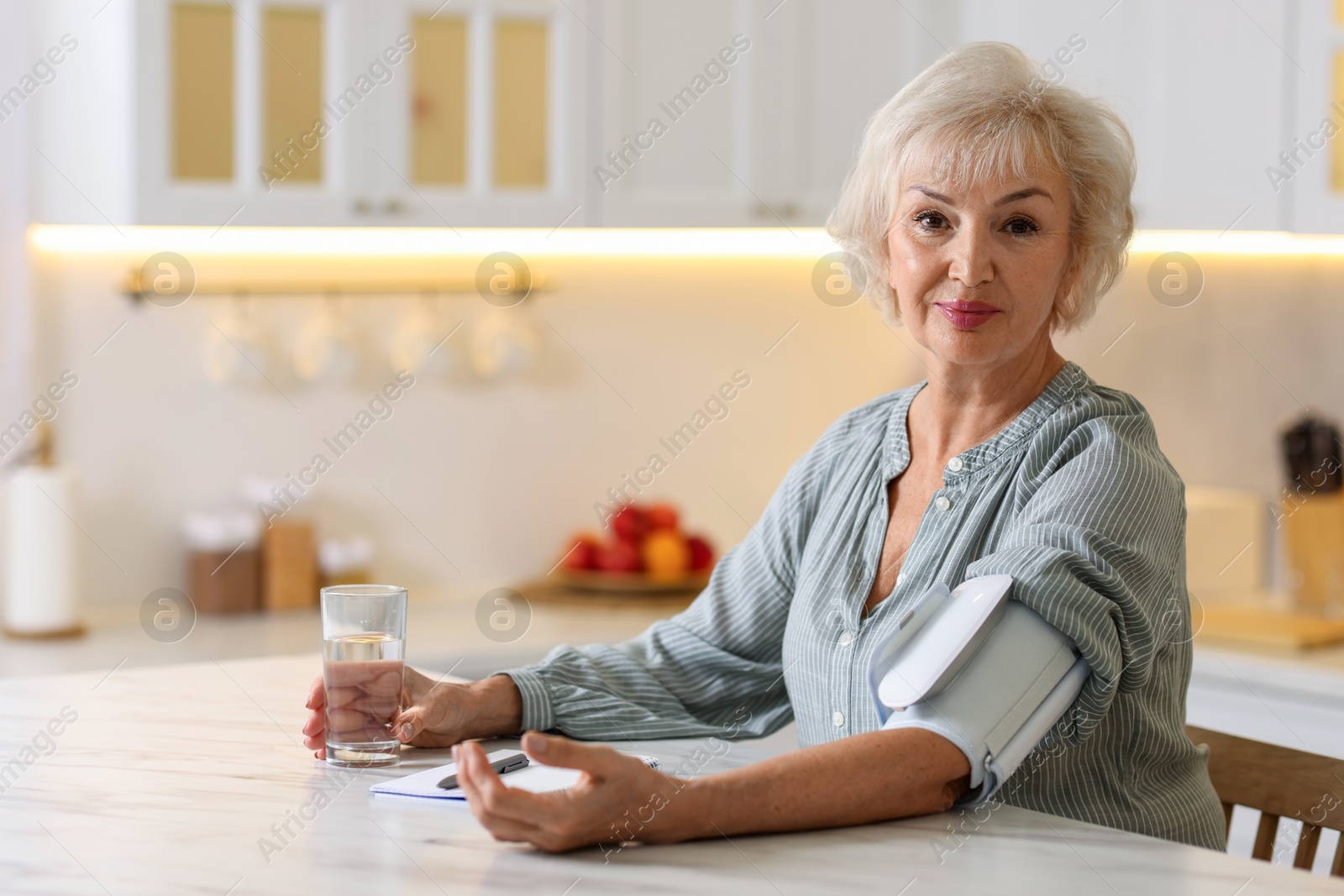 Photo of Senior woman measuring blood pressure at table in kitchen. Space for text