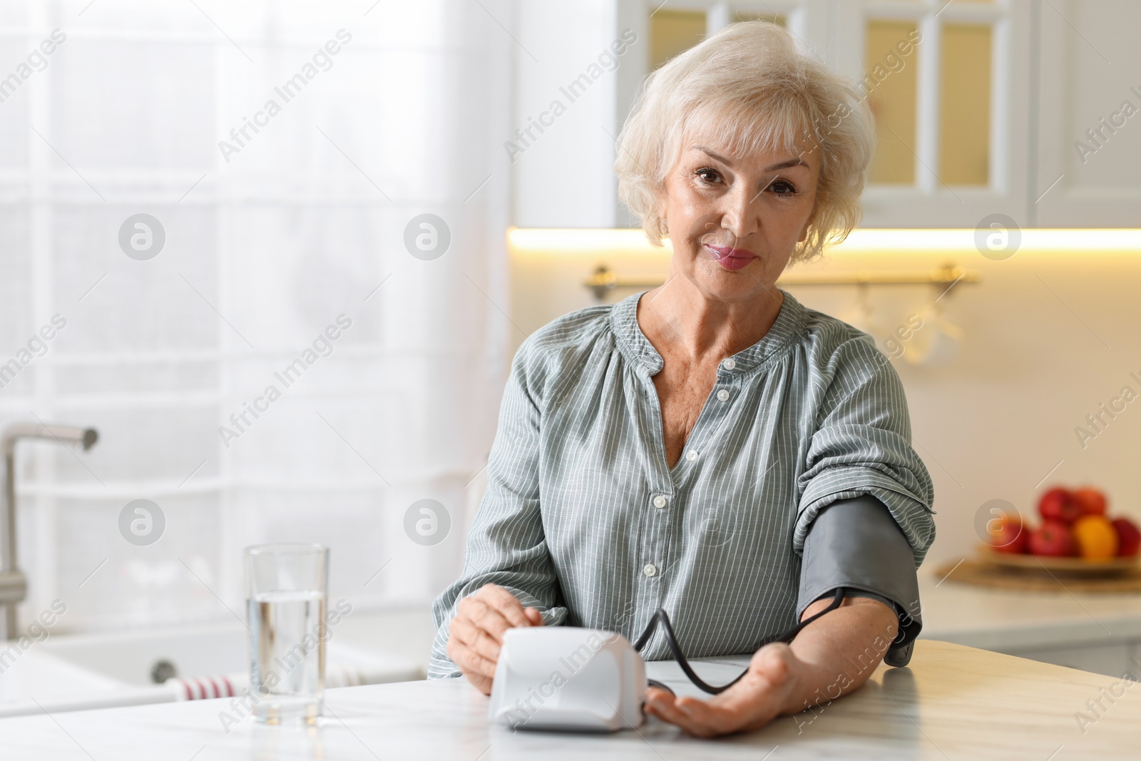 Photo of Senior woman measuring blood pressure at table in kitchen. Space for text