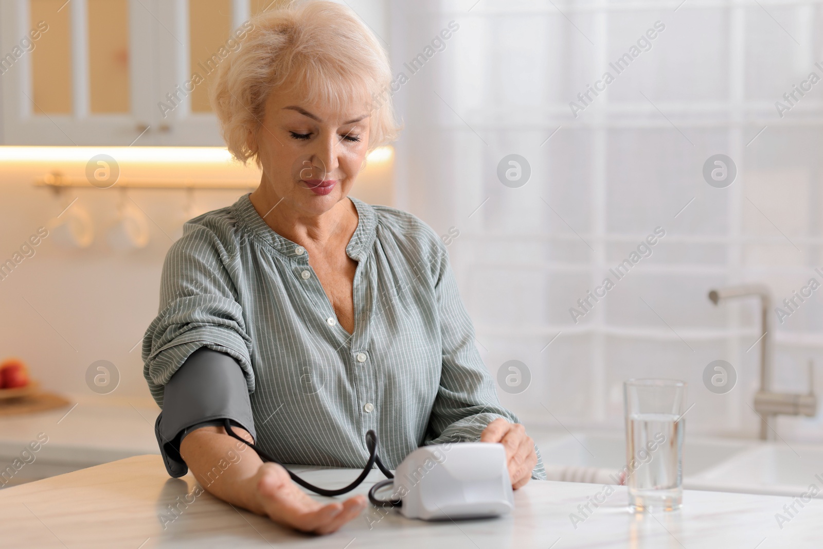 Photo of Senior woman measuring blood pressure at table in kitchen. Space for text