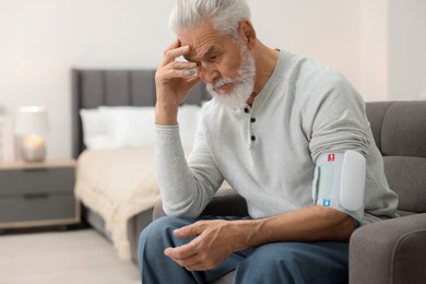 Photo of Worried senior man measuring blood pressure in armchair at home