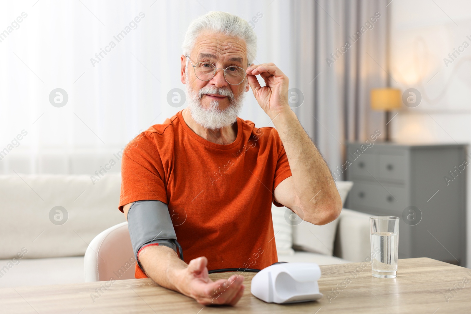 Photo of Senior man measuring blood pressure at table indoors