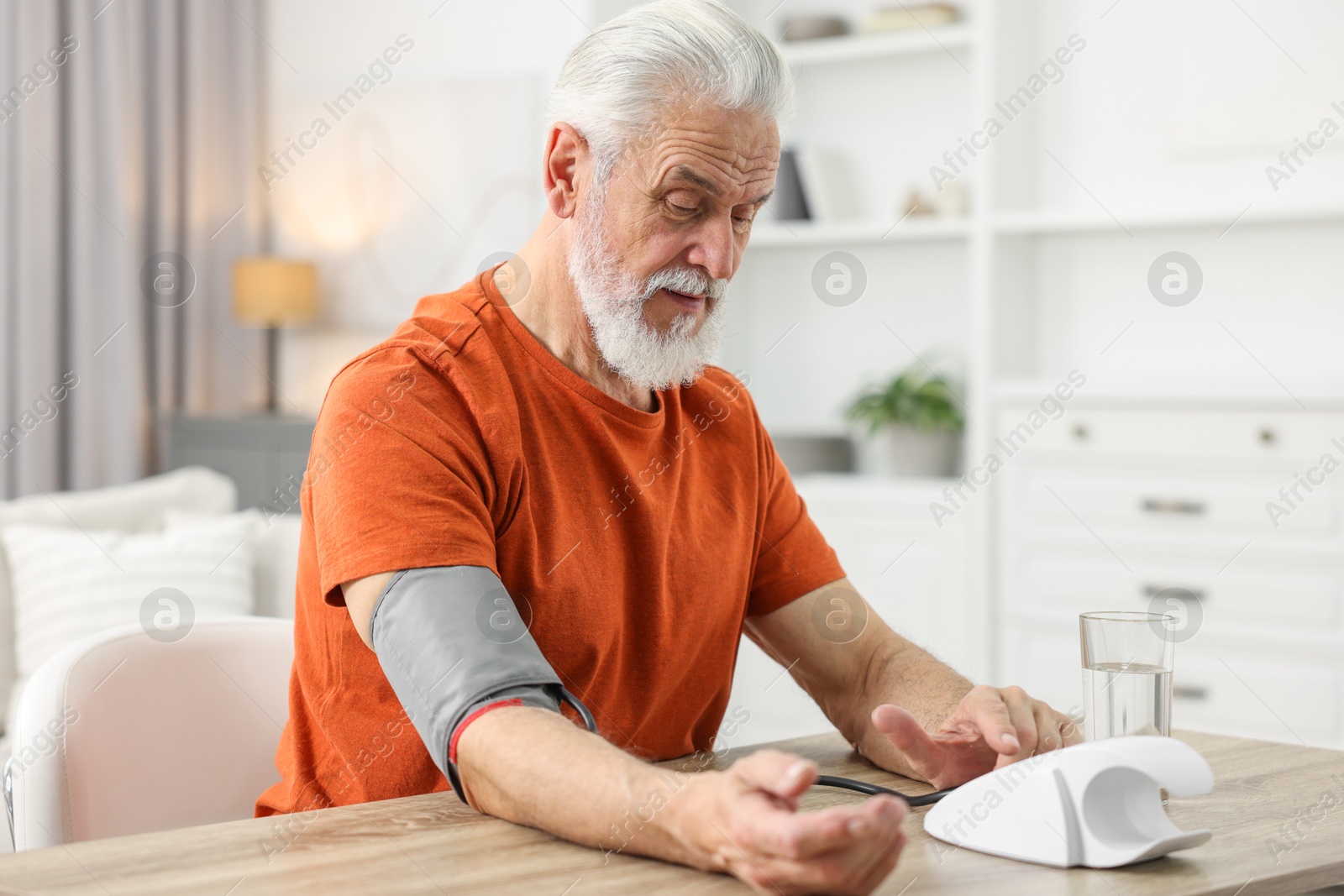 Photo of Senior man measuring blood pressure at table indoors