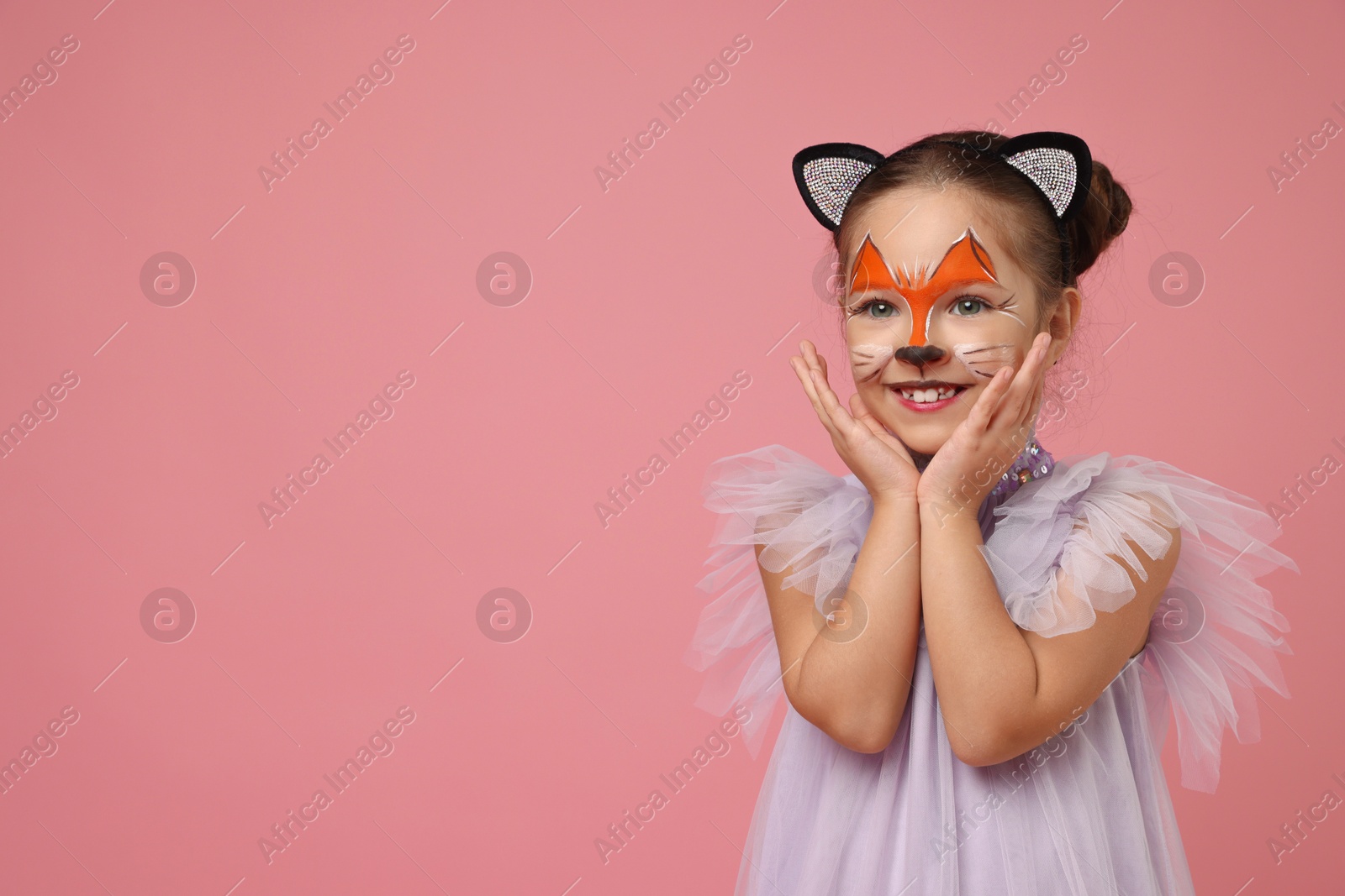 Photo of Cute girl with painted face and ears as cat on pink background, space for text