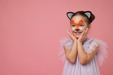 Photo of Cute girl with painted face and ears as cat on pink background, space for text