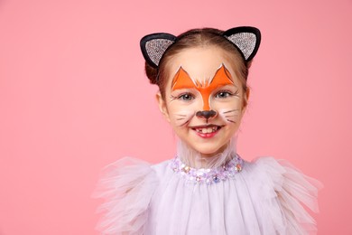 Photo of Cute girl with painted face and ears as cat on pink background, space for text