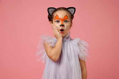 Photo of Cute girl with painted face and ears as cat on pink background