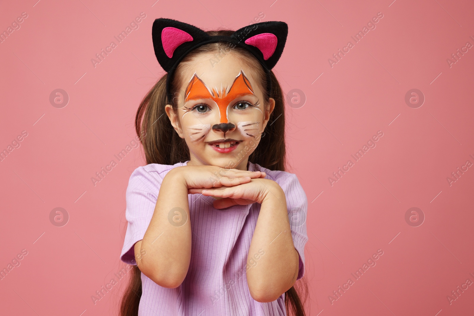 Photo of Cute girl with painted face and ears as cat on pink background, space for text