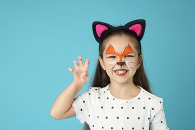 Photo of Cute girl with painted face and ears as cat on light blue background, space for text