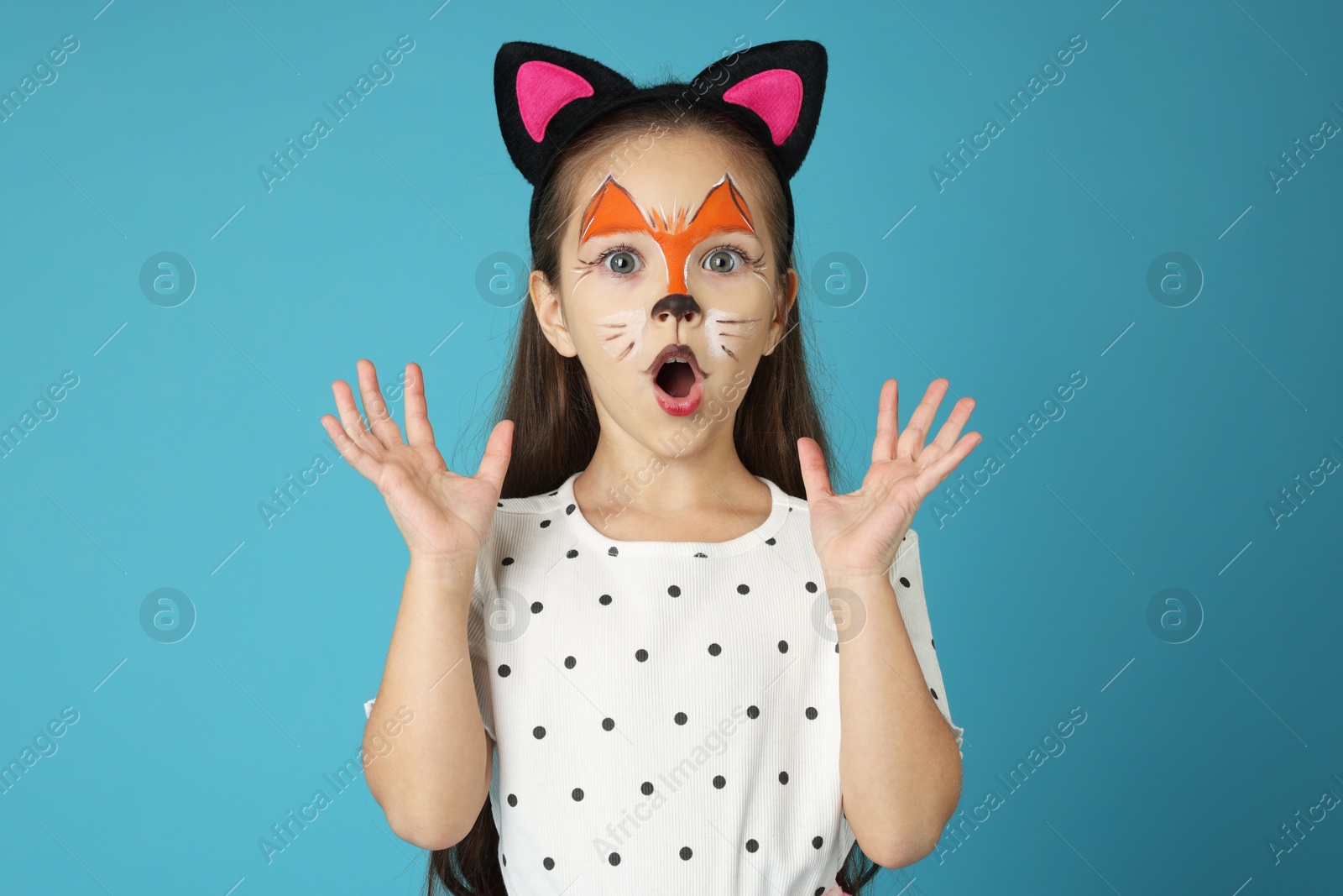 Photo of Cute girl with painted face and ears as cat on light blue background