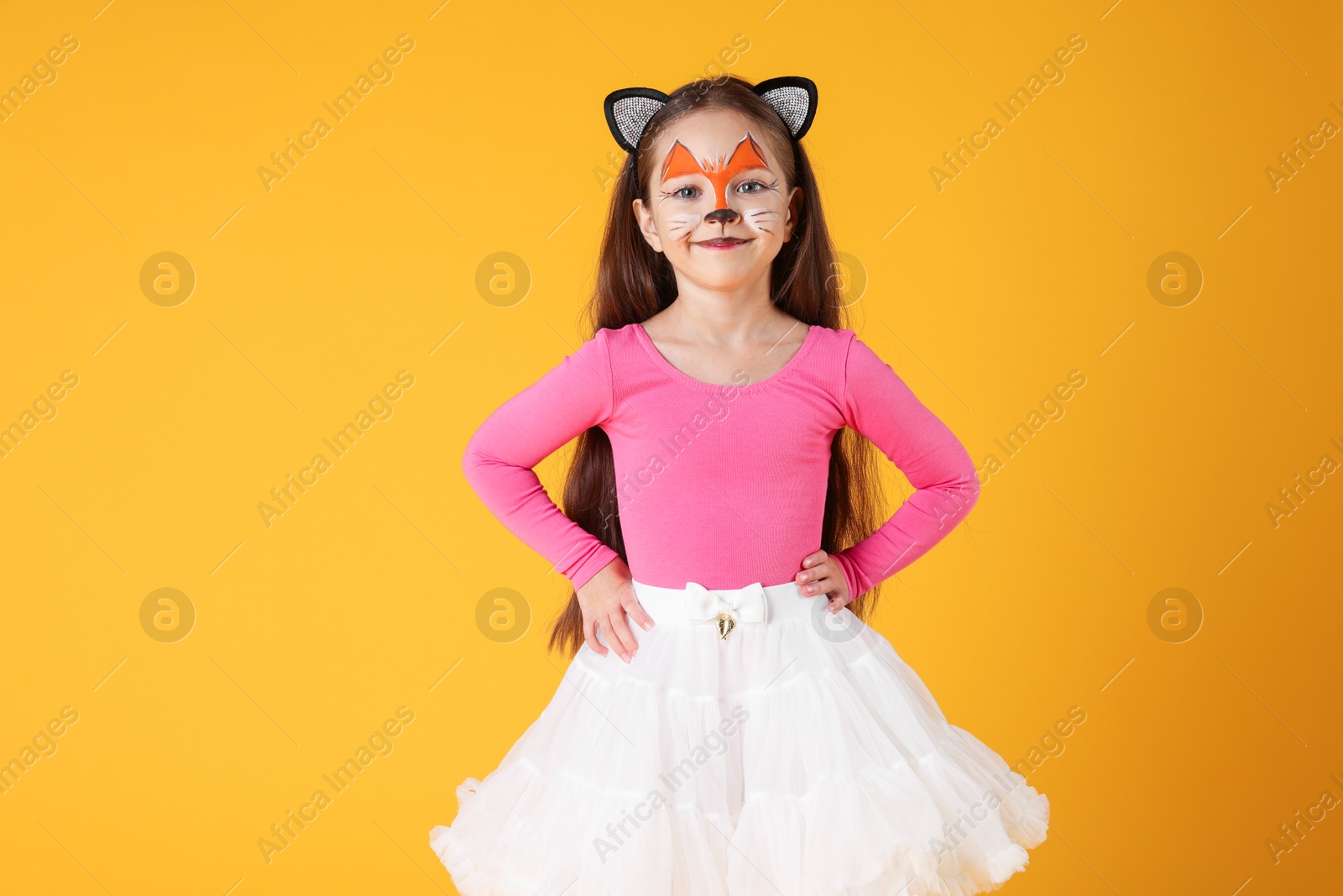 Photo of Cute girl with painted face and ears as cat on orange background