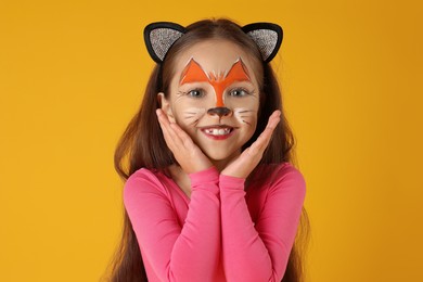 Photo of Cute girl with painted face and ears as cat on orange background