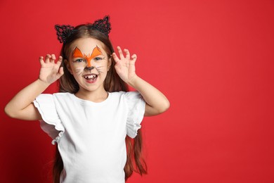 Cute girl with painted face and ears as cat on red background, space for text