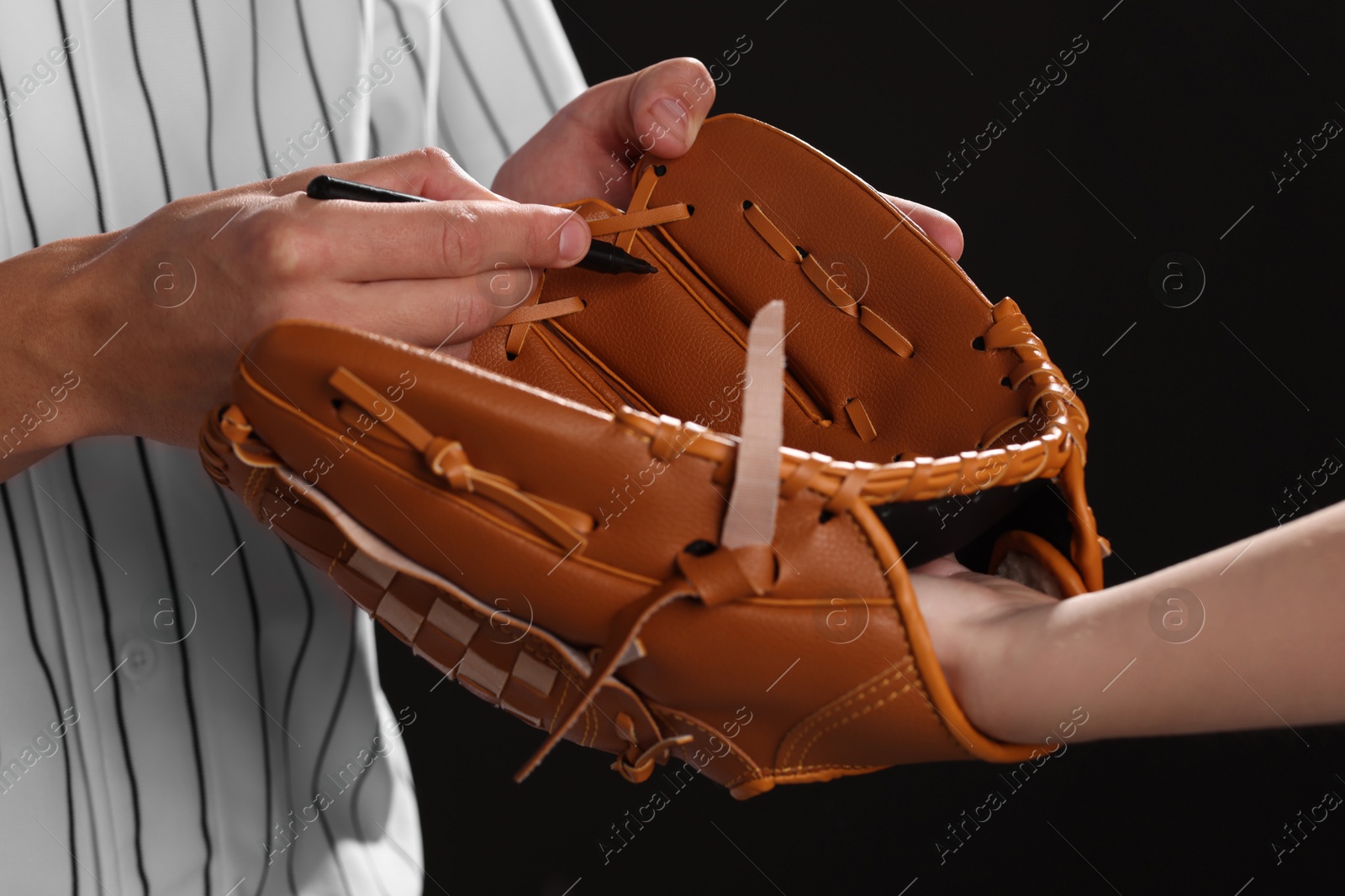 Photo of Baseball player signing autograph on leather glove against black background, closeup