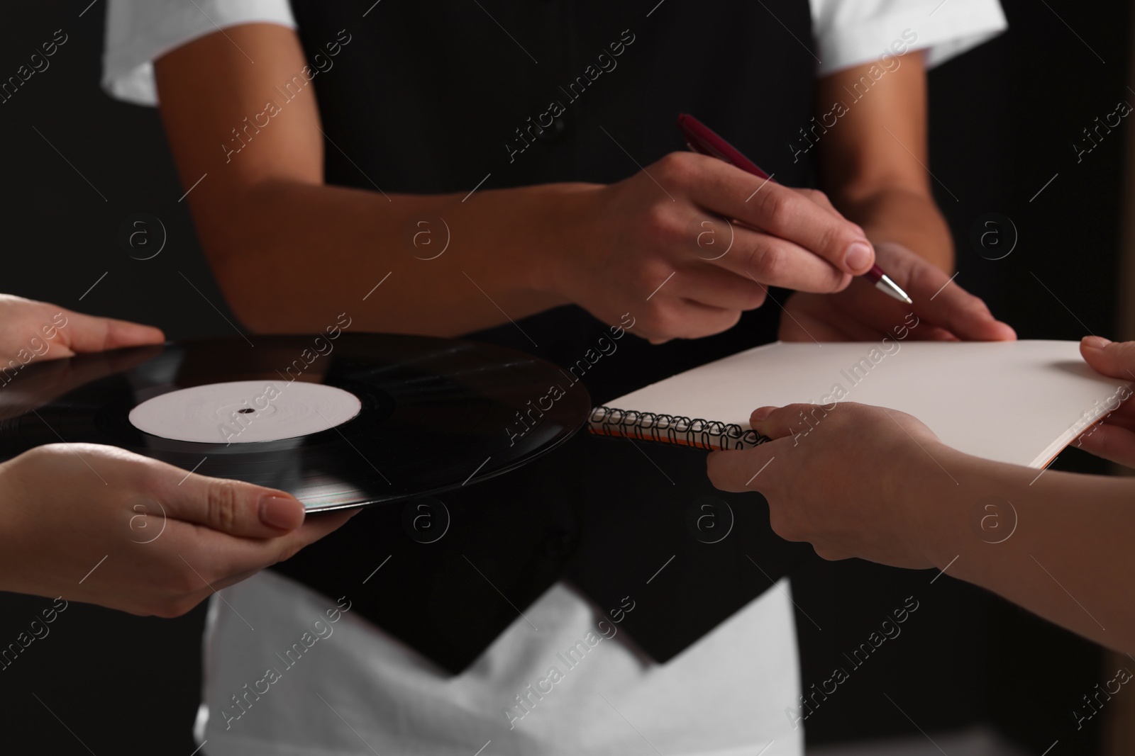 Photo of Singer signing autograph in notebook on black background, closeup