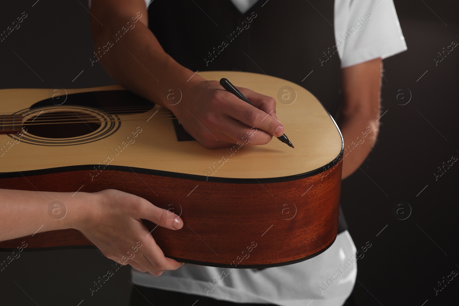 Photo of Musician signing autograph on guitar against black background, closeup