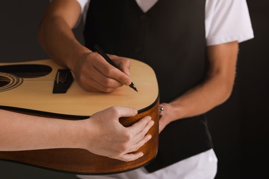 Photo of Musician signing autograph on guitar against dark background, closeup