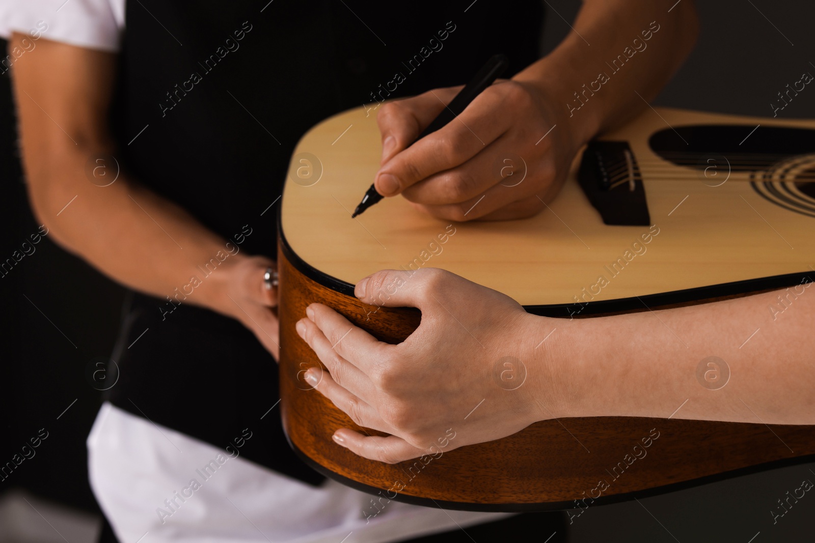 Photo of Musician signing autograph on guitar against dark background, closeup