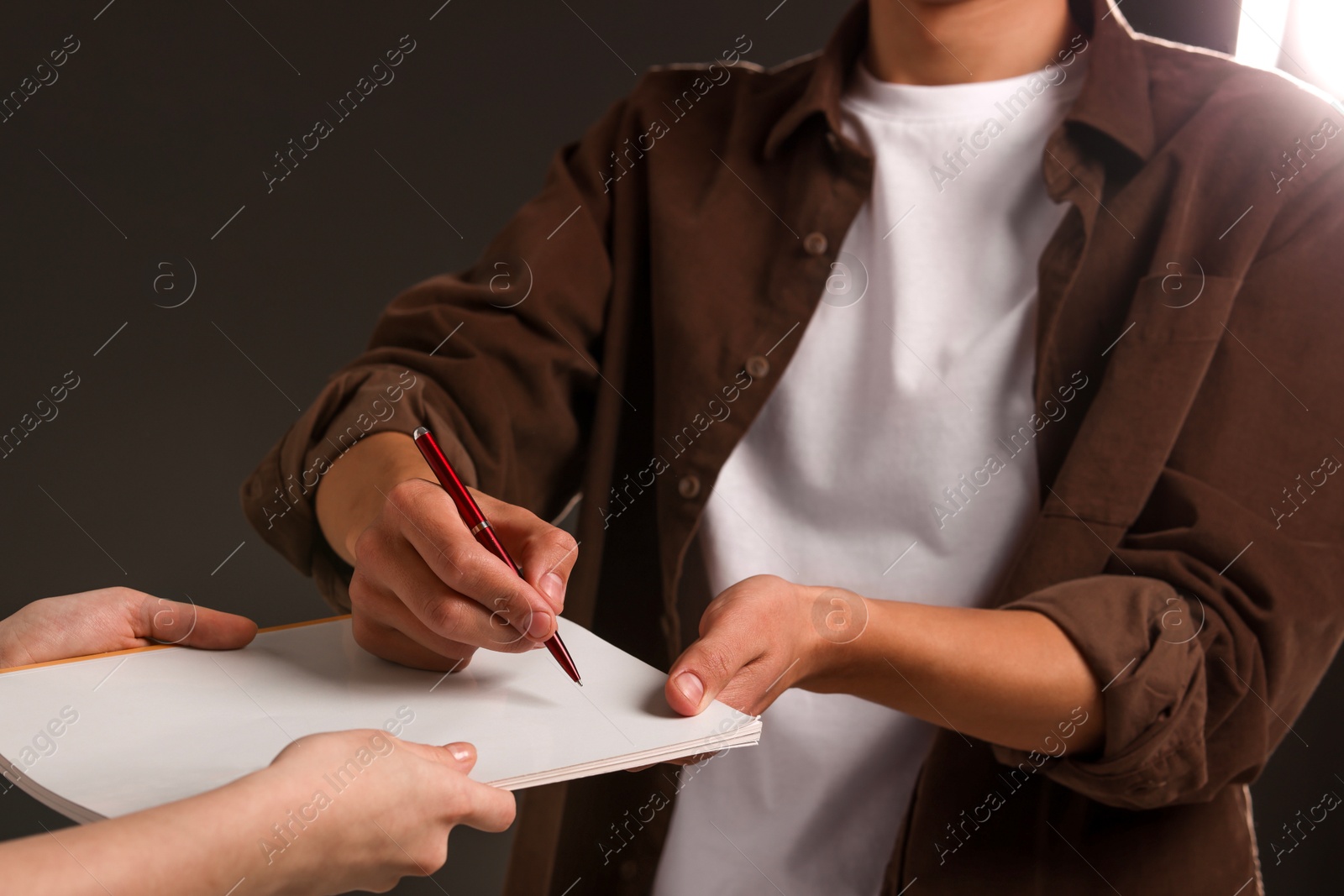 Photo of Man signing autograph in notebook on dark background, closeup