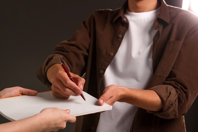 Photo of Man signing autograph in notebook on dark background, closeup