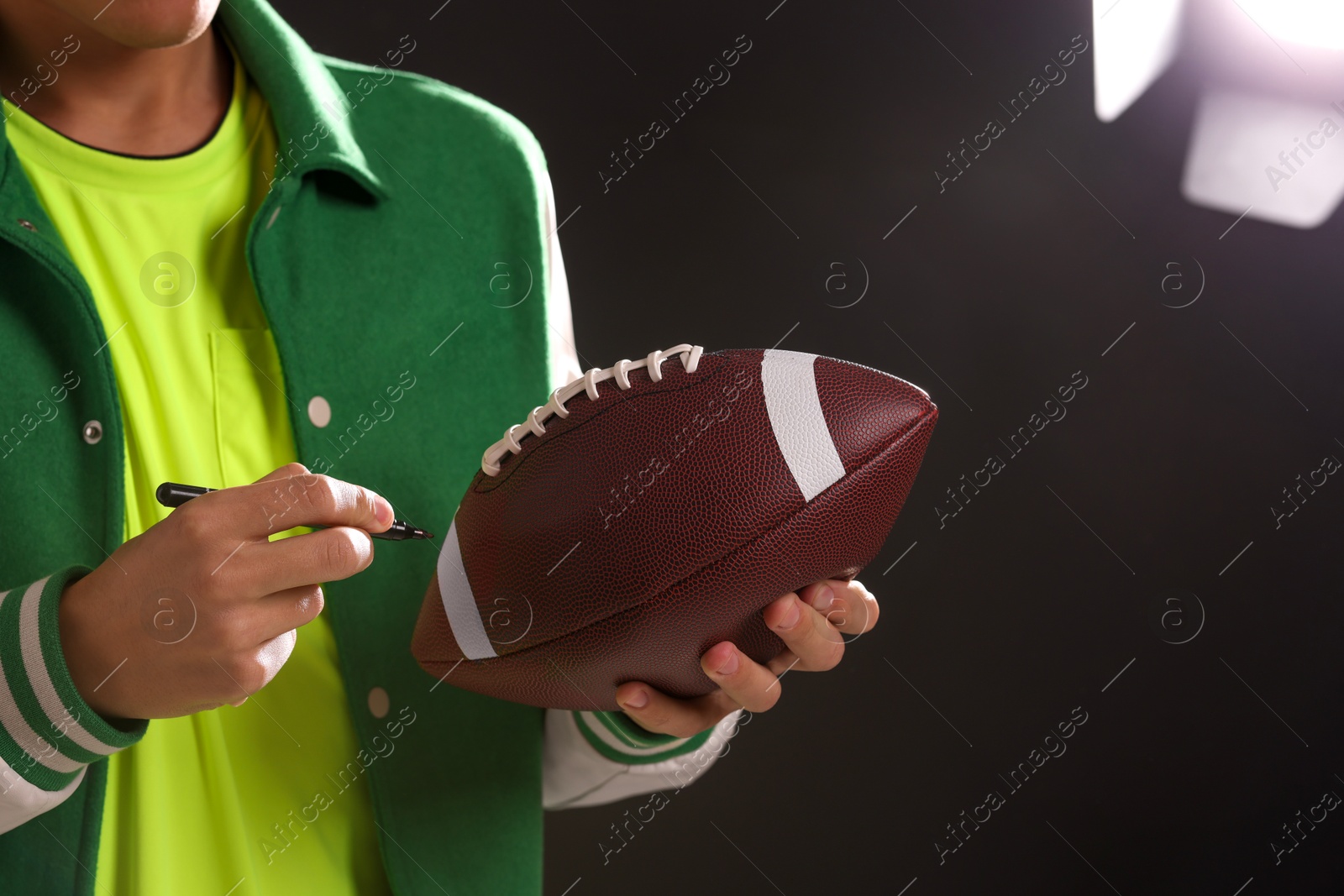 Photo of Professional player signing autograph on American football ball against dark background, closeup. Space for text