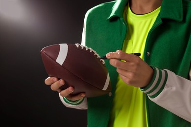 Photo of Professional player signing autograph on American football ball against dark background, closeup