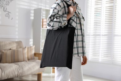 Photo of Woman with blank black shopper bag indoors, closeup. Mockup for design