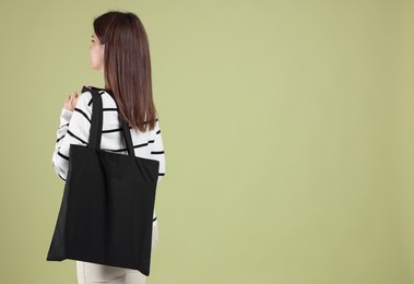 Photo of Woman with blank black shopper bag on color background, back view. Mockup for design