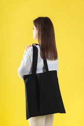 Photo of Woman with blank black shopper bag on yellow background, back view. Mockup for design