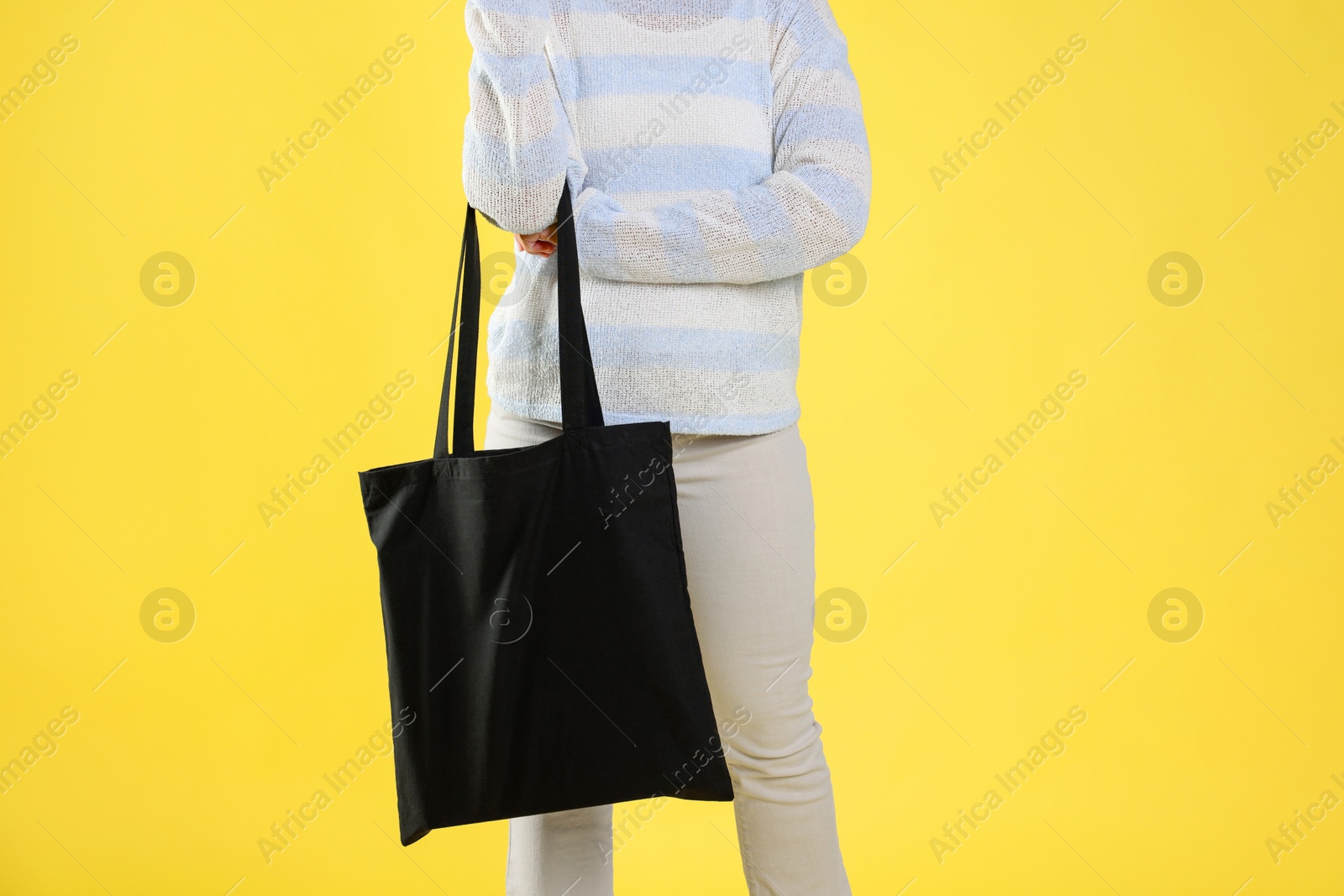 Photo of Woman with blank black shopper bag on yellow background, closeup. Mockup for design